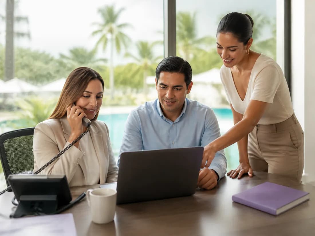 Tres personas del equipo comercial de un hotel revisan juntas una laptop mientras una de ellas atiende una llamada.